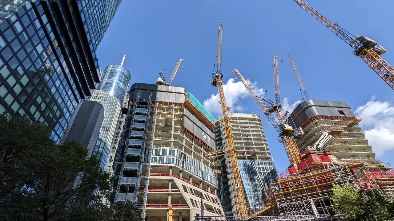Tower cranes beside high-rise buildings under construction, seen from below